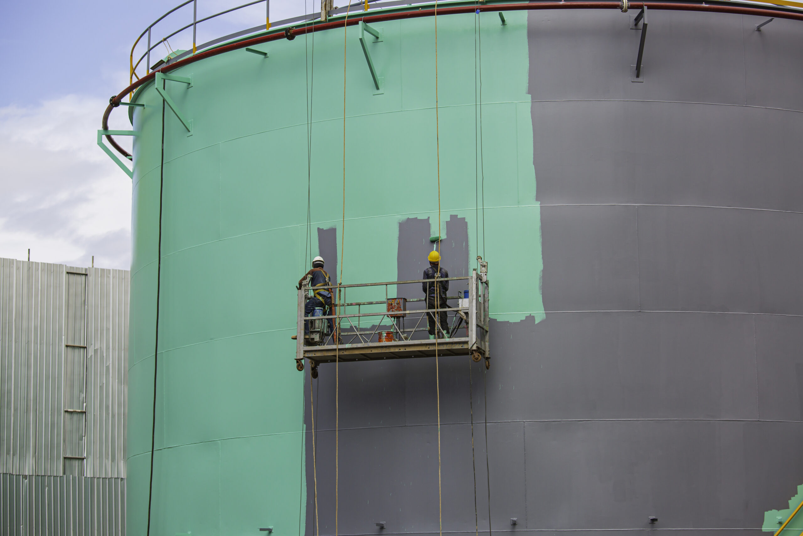 The male worker takes the cable car holding an industrial painting brush used for shell plate tank oil surface surface green color coating.