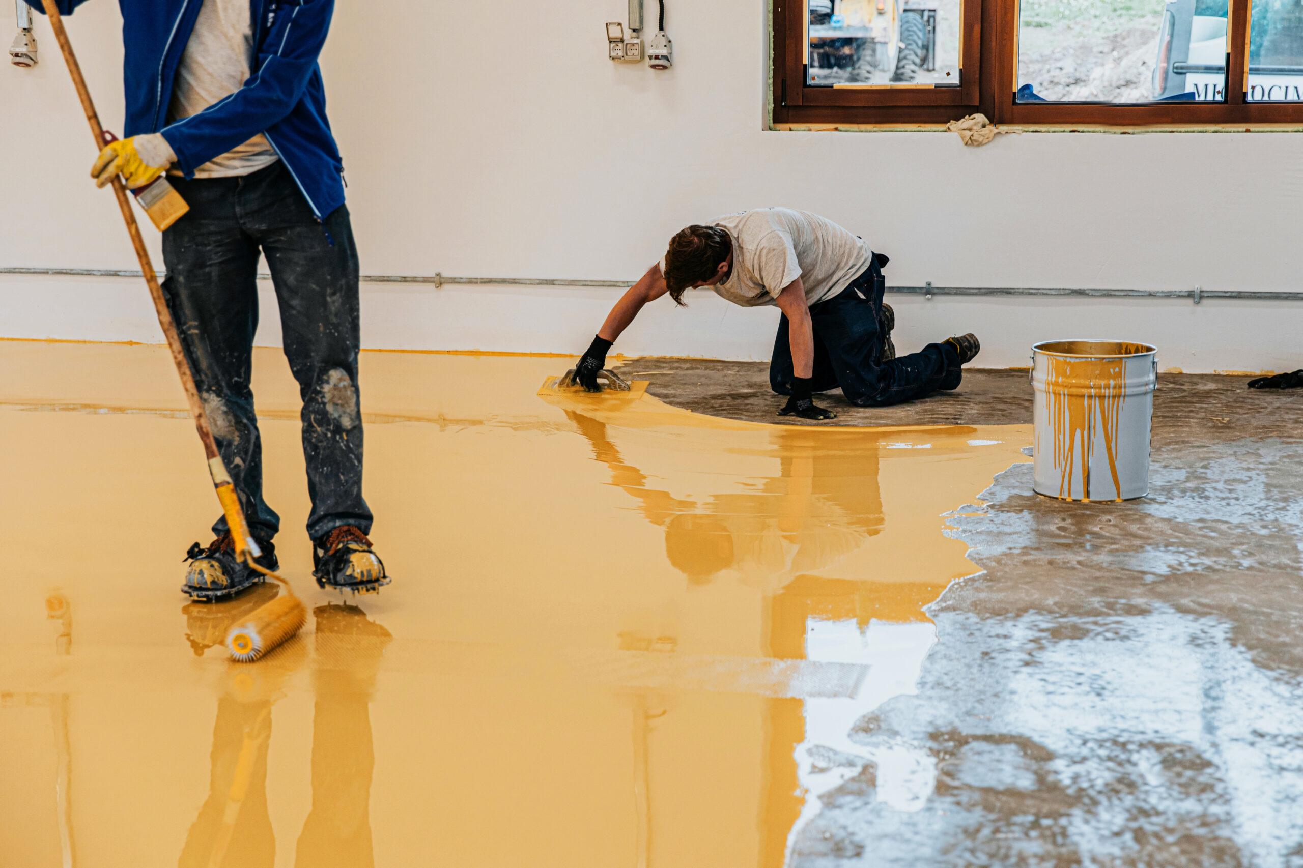 Worker, coating floor with self-leveling epoxy resin in industrial workshop.